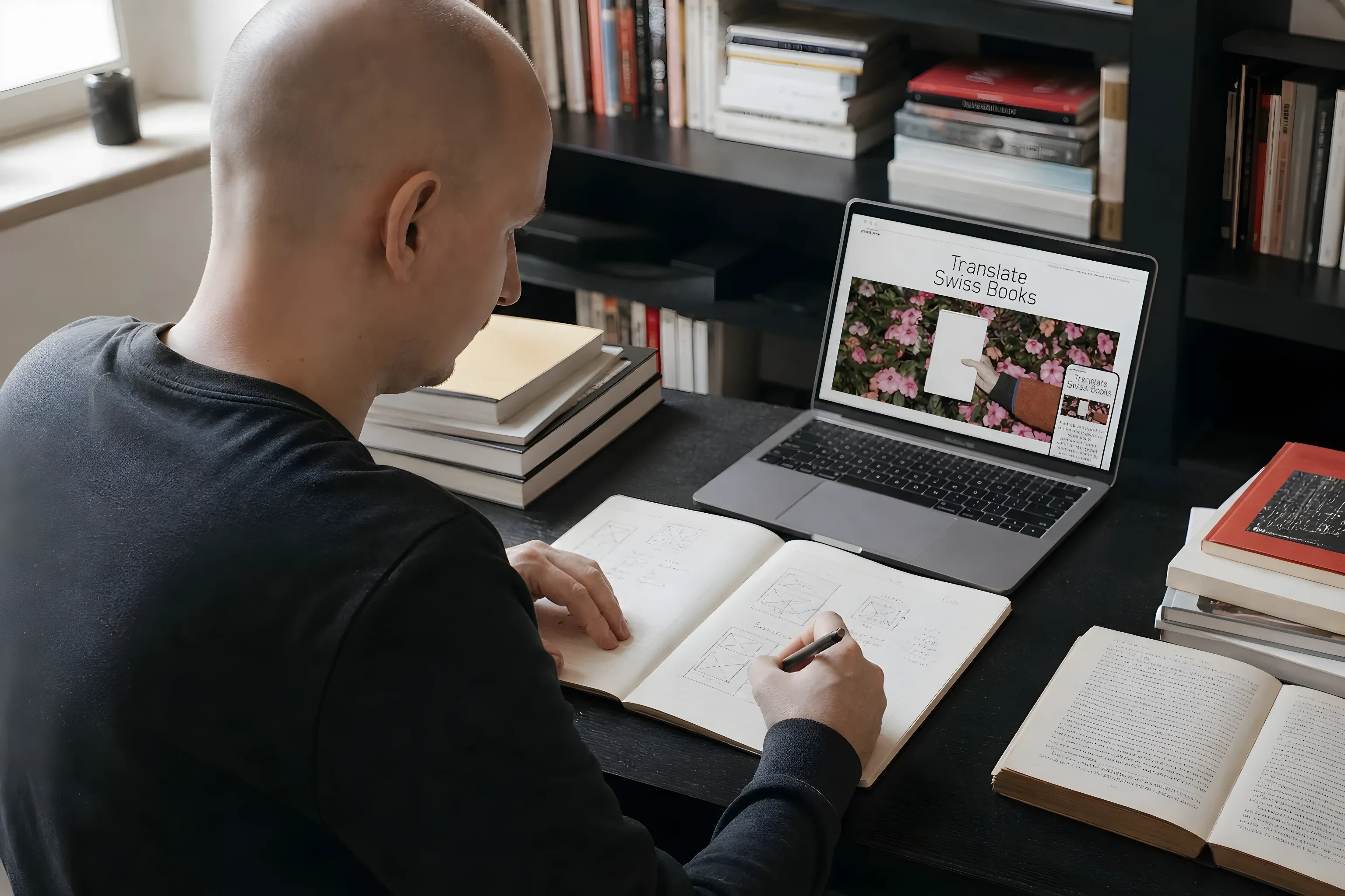 Simon sketching layouts in a notebook next to the Translate Swiss Books site
